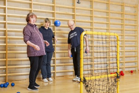 Kolme liikkujaa heittää palloja kohti maalia liikuntasalissa